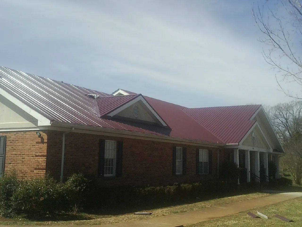 Red metal roof with gabled entries on a long brick building, from a Hail Damage Roof Repair job in Clifton
